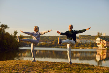 Active sporty senior couple doing stretching exercising in nature. Happy smiling elderly man and woman in sportswear having sport workout in park. Outdoors training and fitness in retirement concept. - obrazy, fototapety, plakaty