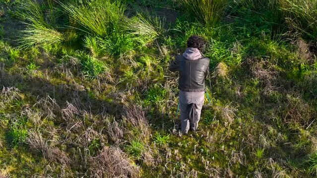 Above View Of A Photographer Keeping His Tripod And Camera In Grassy Nature Landscape. Aerial Shot