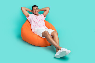 Full length photo of satisfied man wear pink polo lay on bean bag holding hands behind head...
