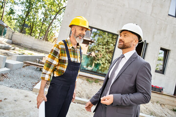 merry cottage builder and architect in suit and overalls with blueprint discussing construction
