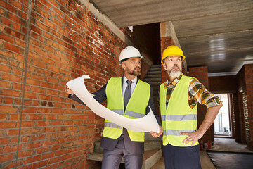 handsome bearded cottage builder and architect working on construction site with blueprint