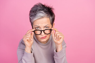 Photo of charming retired woman hold glasses suspiciously looking watching camera isolated on pink...