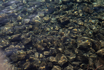 Sea rocky bottom under transparent blue water. Clear turquise lake surface rippled with sun ray reflection.