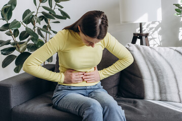 Close up of upset young woman suffering from menstrual pain. Girl with hands squeezing belly having...