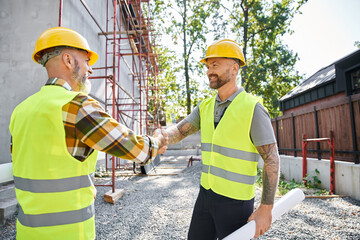 cheerful construction workers shaking their hands and smiling at each other, cottage builders - 742714352