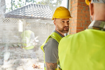 focus on bearded worker in safety helmet talking to his colleague on construction site, builders