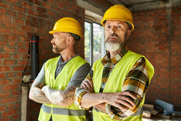 dedicated bearded cottage builders in safety helmets and vests posing together with arms crossed