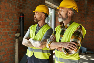 dedicated bearded cottage builders in safety helmets and vests posing together with arms crossed