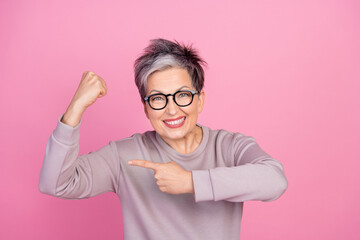 Photo of funny strong retired woman raise arm show strength biceps muscles isolated on pink color...