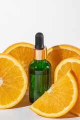 Vitamin C serum in cosmetic green bottle with dropper, sliced oranges on white background. Organic SPA cosmetics with herbal ingredients.