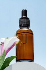 A brown dropper bottle of face oil displayed on a pedestal against a blue background with pink alstromeria flower. cosmetic package , unbranded mockup