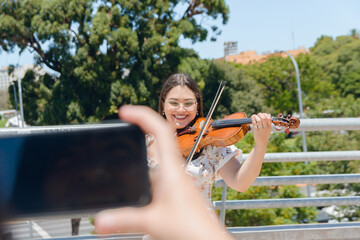 woman filming busker female violinist with her phone outdoors