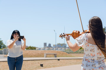 rear view of female violinist content creator playing violin while being filmed for social media