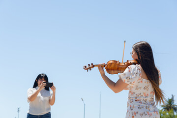 rear view of female violinist content creator playing violin while being filmed for social media