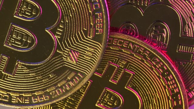 Close-up of gold cryptocurrency bitcoins glowing pink and blue neon light slowly rotating background. Digital crypto coins. Exchange online market.