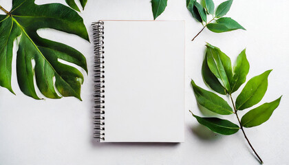 Empty rustic style notepad with green leaves on a table. Blank white mockup sketchbook on white background, free space. Top view, copy space for text or advertisement. - obrazy, fototapety, plakaty