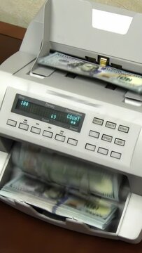 Vertical video of a money counting machine counts $10,000 in new $100 bills.  	