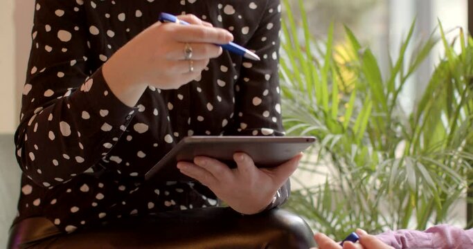 Close-up of two woman with tablet talking during informal Work Meeting: Two Colleagues Discussing Business Matters in Relaxed Setting. Casual workplace interactions. No face people, hands gesturing.
