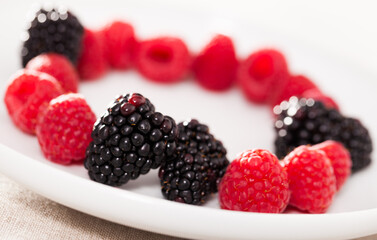 Raspberries and blackberries laid out on a white plate in circle