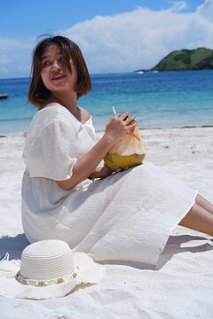 Portrait image of a beautiful Asian woman holding a fresh coconut and enjoying it on Lombok beach
