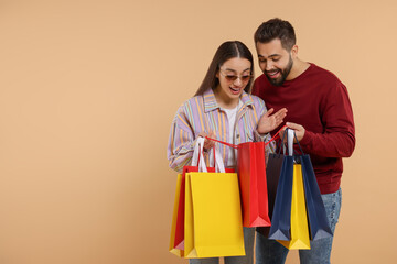 Man showing shopping bag with purchase to his girlfriend on beige background. Space for text