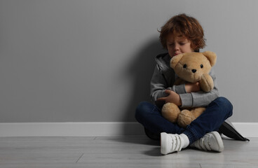 Child abuse. Upset boy with toy sitting on floor near grey wall, space for text