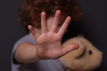 Child abuse. Boy with toy making stop gesture near grey wall, selective focus