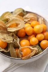 Ripe physalis fruits with calyxes in bowl on white table, closeup
