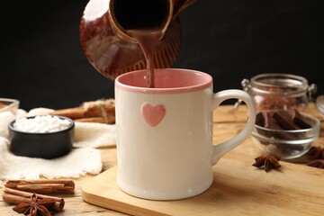 Pouring tasty hot chocolate into cup at wooden table, closeup