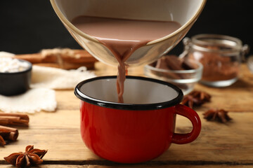Pouring tasty hot chocolate into cup at wooden table, closeup