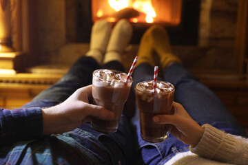 Couple with glasses of hot cocoa near fireplace at home, closeup