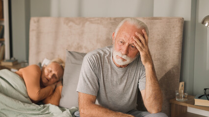 Senior man sitting on bed looking worried