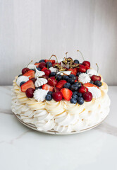 Pavlova cake with whipped cream cheese, chocolate sauce, fresh strawberry, blueberry and raspberry, decorated with meringues on plain background