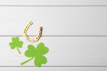 St. Patrick's day. Golden horseshoe and green decorative clover leaves on white wooden table, flat lay. Space for text