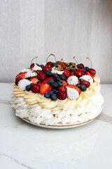 Pavlova cake with whipped cream cheese, chocolate sauce, fresh strawberry, blueberry and raspberry, decorated with meringues on plain background