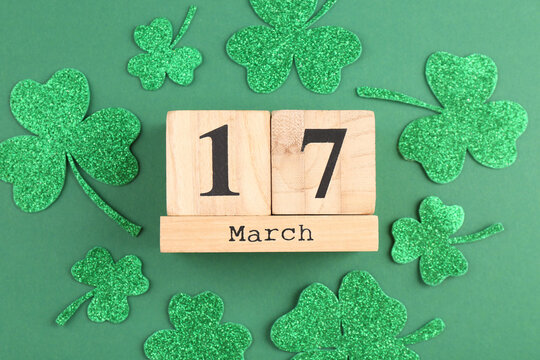 St. Patrick's day - 17th of March. Block calendar and decorative clover leaves on green background, flat lay