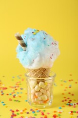 Sweet cotton candy in waffle cone on yellow background, closeup