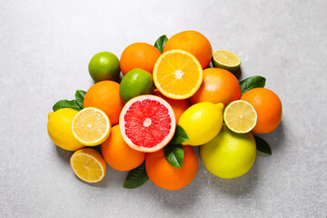 Pile of different fresh citrus fruits and leaves on grey textured table, flat lay