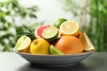 Different fresh citrus fruits and leaves on grey table against blurred background, closeup