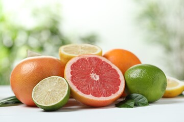 Different fresh citrus fruits and leaves on white table against blurred background, closeup