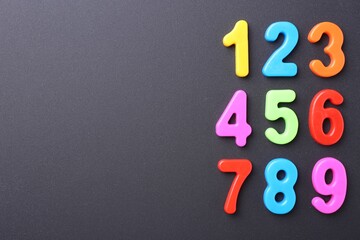 Colorful numbers on dark gray background, flat lay. Space for text