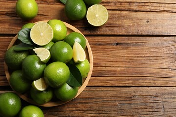 Fresh limes and green leaves on wooden table, top view. Space for text