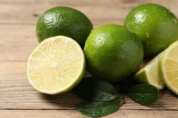 Fresh ripe limes and green leaves with water drops on wooden table, closeup