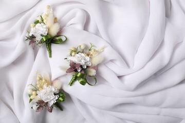 Stylish boutonnieres on white silk, flat lay. Space for text