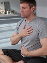 Yoga fitness man doing breathing exercises, holding one hand on heart another on stomach. Deep...