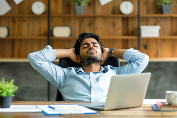 Business bookkeeper financial accountant feels tired but satisfied after completing big work amount. Relaxed young Indian man with hands behind head sitting at office desk with laptop computer