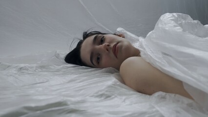 Female in underwear laying on the bed in the studio. Young woman seminude in lingerie laying posing...