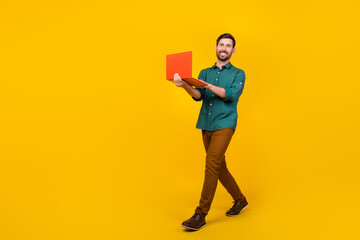 Full size photo of successful guy dressed dotted shirt brown trousers hold laptop go empty space isolated on vivid yellow color background