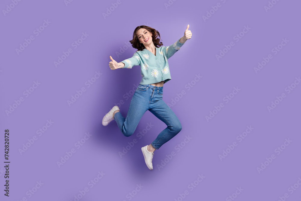 Poster Full length photo of funky positive woman wear flower print cardigan showing two thumbs up jumping high isolated purple color background