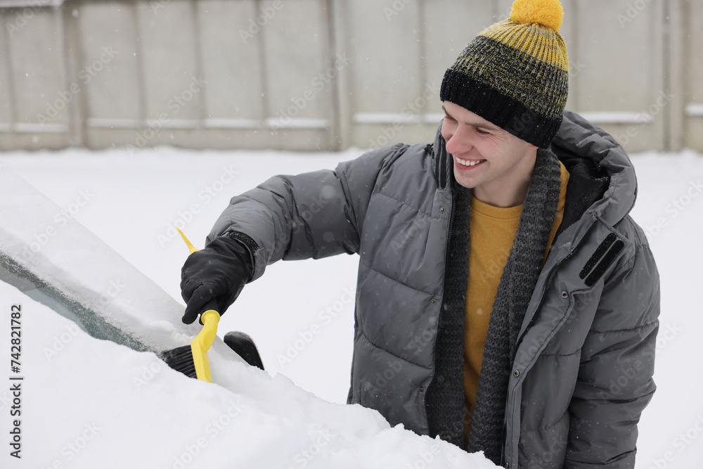 Wall mural man cleaning snow from car windshield outdoors